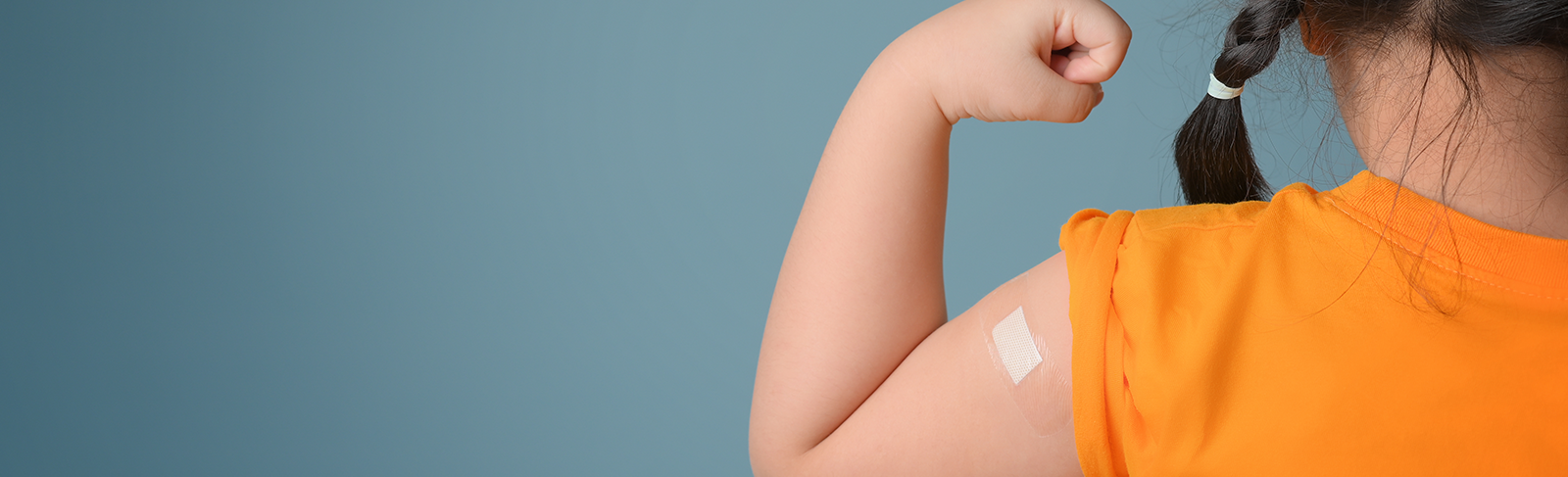 Child showing off their vaccinated arm with blue background