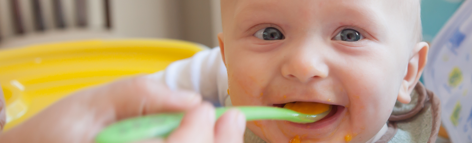 Baby with blue eyes eating off a spoon.