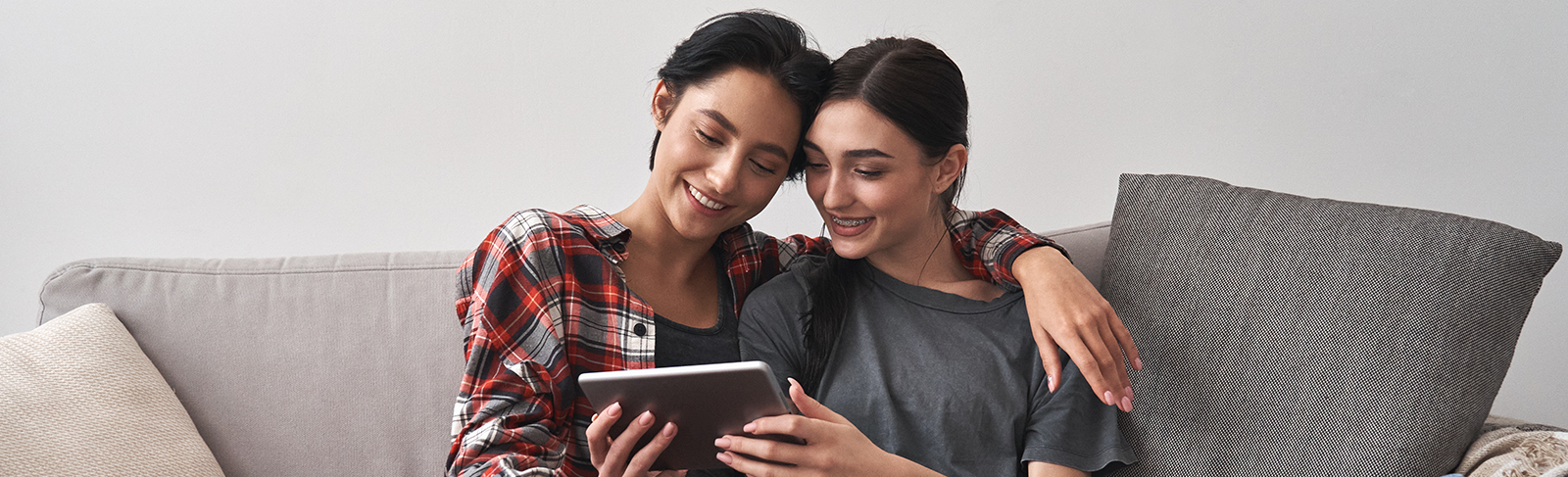 Two people sitting on the couch cuddling and looking at a tablet.
