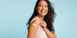 A person smiling with shirt sleeve rolled up to expose bandage on upper arm